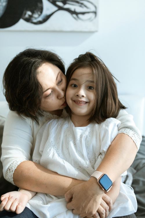 Adult woman hugs a child on her lap; she wears a smartwatch on her wrist.