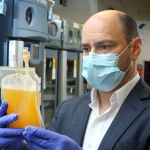 Dr. Shmuel Shoham wears a blue surgical mask and holds a medical bag of plasma in gloved hands